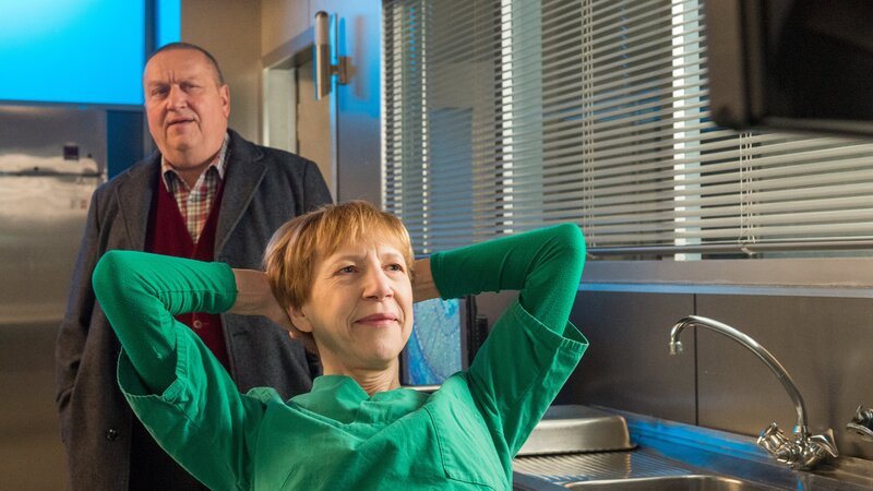 Kriminalhauptkommissar Jan Reuter (Udo Kroschwald, l.) erwischt Dr. Helene Sturbeck (Katharina Blaschke, r.) beim Hören von Dudelsack-Musik; nach einem Wortgefecht erfährt Reuter, dass die Todesursache ein Schlag mit einem Kantholz war. – Bild: ZDF /​ Meyerbroeker