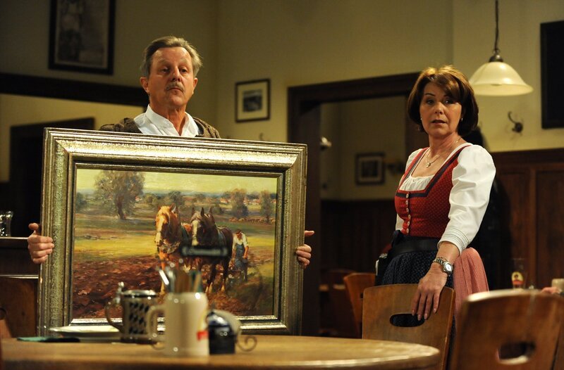 Schattenhofer preist sein Gemälde bei Rosi an. Von links: Bürgermeister Schattenhofer (Werner Rom) und Rosi Brunner (Brigitte Walbrun). – Bild: BR/​Marco Orlando Pichler