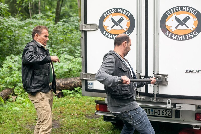 Hubert (Christian Tramitz, l.) und Yazid (Hannes Ringlstetter, r.) brechen den Kühlwagen der Metzgerei Semmling, der schon seit einiger Zeit auf einem Waldparkplatz steht, mit Gewalt auf. – Bild: ARD/​TMG/​Chris Hirschhäuser