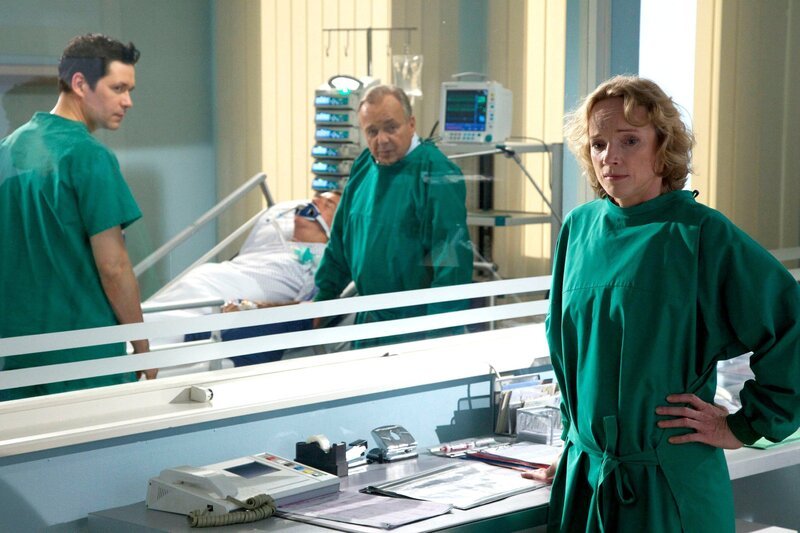 Horst Kramer (Wilfried Dziallas, liegend) hat einen weiteren Schlaganfall erlitten. Er muss dringend operiert werden, doch sein Zustand ist so kritisch, dass die Operation ein enormes Risiko birgt. Prof. Simoni (Dieter Bellmann, rechts) und Dr. Philipp Brentano (Thomas Koch, links) haben sich bei seiner Tochter Claudia (Claudia Geisler, vorn) nach einer Patientenverfügung erkundigt. Doch diese gibt es nicht. Claudia hat eine Vorsorgevollmacht – im Notfall liegt die Entscheidung ganz allein bei Claudia. – Bild: MDR/​Wernicke