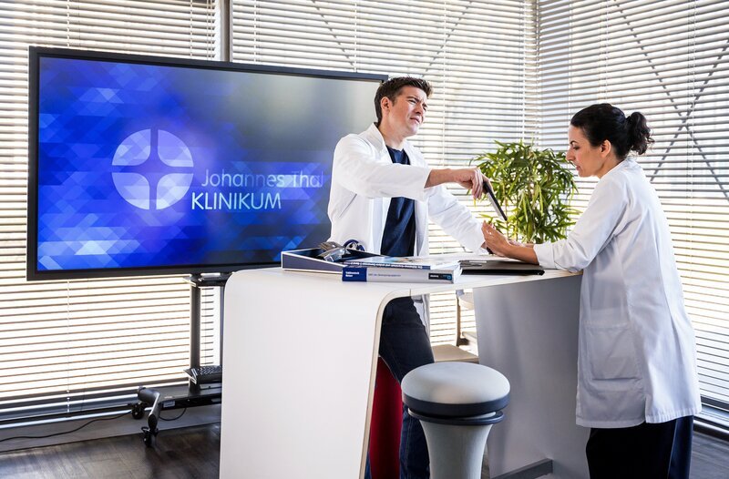 Dr. Ben Ahlbeck (Philipp Danne, l.) zeigt seiner Frau Dr. Leyla Sherbaz (Sanam Afrashteh, r.) den Kindergartengruppenchat und erzählt ihr vom toten Meerschweinchen aus dem Kindergarten ihrer Tochter Raya. – Bild: ARD/​Michael Kremer