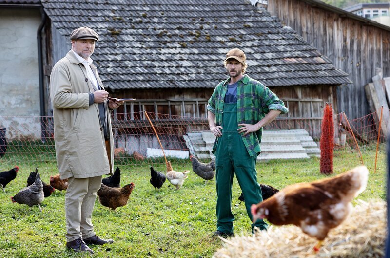 Wer stiehlt Bauer Brus (Kevin Brand, re.) die Hühner? Inspektor Sifkovits (Thomas Stipsits, li.) soll den Dieb schnappen – und stolpert stattdessen über einen Mordfall. – Bild: Mona Film/​Victoria Herbig