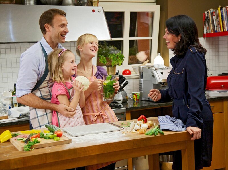 Dr. Martin Stein (Bernhard Bettermann) und seine Tochter Marie (Henriette Zimmeck, 3.v.li.) sind so glücklich darüber, dass Elena Eichhorn (Cheryl Shepard, re.) und ihre Tochter Sophie (Leni Johanna Trost, 2.v.li.) endlich eingezogen sind, dass Martin sofort den nächsten Schritt gehen möchte: Er will Elena einen Heiratsantrag machen. – Bild: MDR/​Saxonia/​Wernicke