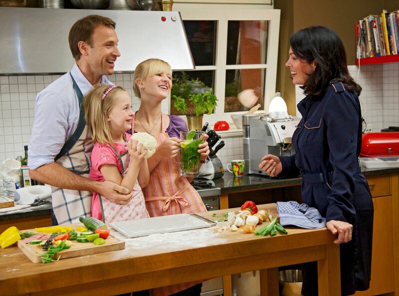 Dr. Martin Stein (Bernhard Bettermann) und seine Tochter Marie (Henriette Zimmeck, 3.v.li.) sind so glücklich darüber, dass Elena Eichhorn (Cheryl Shepard, re.) und ihre Tochter Sophie (Leni Johanna Trost, 2.v.li.) endlich eingezogen sind, dass Martin sofort den nächsten Schritt gehen möchte: Er will Elena einen Heiratsantrag machen. – Bild: MDR/​Saxonia/​Wernicke