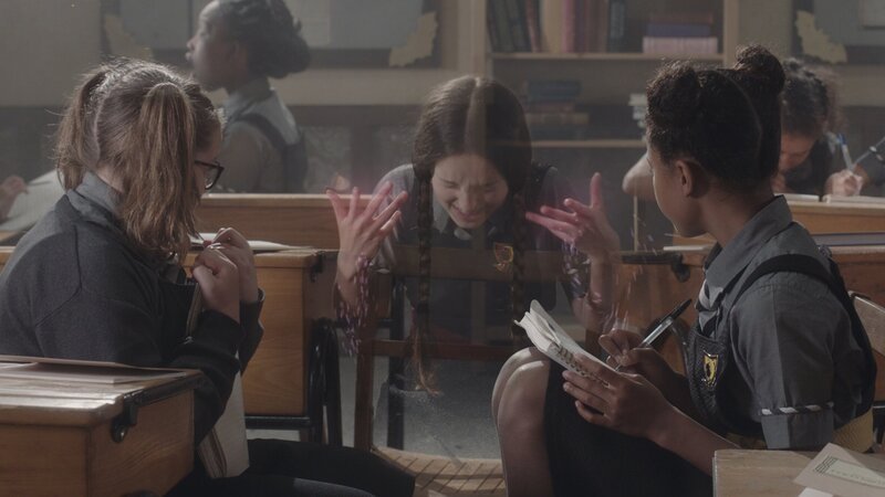 Mildred (Bella Ramsey, Mitte) wendet gerade einen modernen Verschwinde-Zauber an. Unsichtbar will sie im Büro von der Direktorin nach der Schriftrolle mit den Unterschriften suchen. Sie und ihre Freundinnen Maude (Megan Hughes, links) und Edith (Tamara Smart, rechts) vermuten, dass die Unterschriften gefälscht sind. – Bild: BBC/​ZDF Enterprises