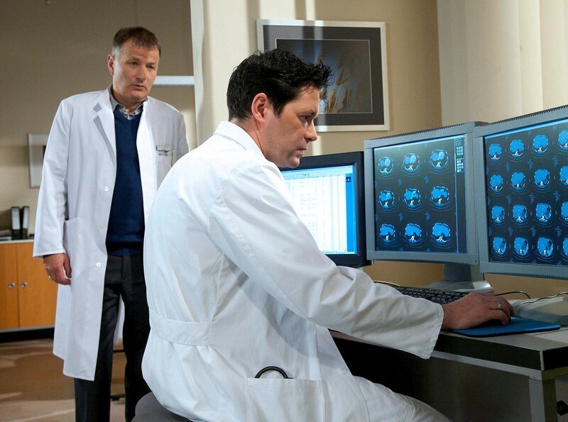 Dr. Philipp Brentano (Thomas Koch, rechts) wertet wieder und wieder die Aufnahmen seines Patienten Wolfgang Voß aus. Herr Voß hat diffuse Beschwerden und scheinbar von allem etwas. Chefarzt Dr. Roland Heilmann (Thomas Rühmann) erkundigt sich nach dem Stand der Untersuchungen. – Bild: MDR/​Wernicke