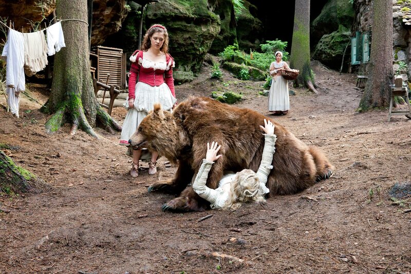Der Bär hat sich von seiner Verletzung erholt und geniesst das Zusammenleben mit Schneeweißchen (Sonja Gerhardt, Mitte) und Rosenrot (Liv Lisa Fries, links). Beim gemeinsamen Tanz stürzt der Bär auf Schneeweißchen. Die Mutter (Jule Ronstedt, rechts) ist sehr erschrocken und will den Bären nicht mehr im Haus haben. – Bild: MDR/​Steffen Junghans