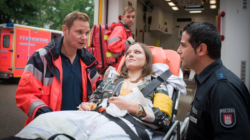 Auch Tina (Emilia von Heiseler, M.) ist zusammengebrochen und wird von Dr. Haase (Fabian Harloff, l.) versorgt. Doch ob es sich um eine Vergiftung handelt, kann er Tarik (Serhat Cokgezen, r.) noch nicht sagen. – Bild: ZDF