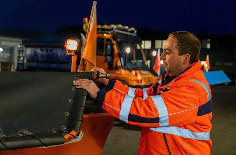Yannik Brüggemann montiert den Schneepflug an das Räumfahrzeug. – Bild: NDR/​dok.weit/​Patrick Stijfhals