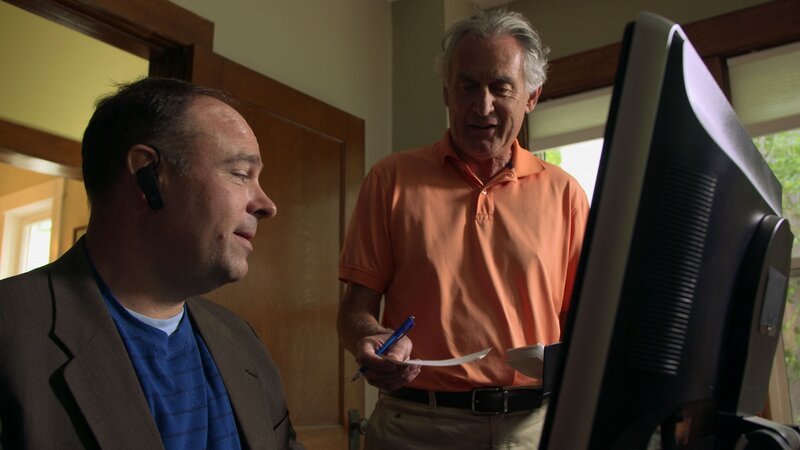 Ein Mann, der einen Stift in der Hand hält, reicht einem anderen Mann, der sitzt, ein Stück Papier. – Bild: Z/​abacus /​ Crime + Investigation