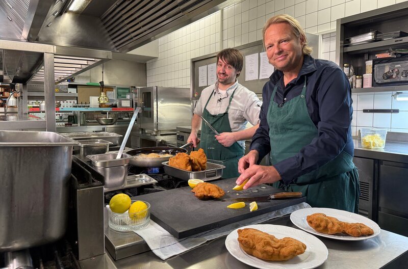 Außen knusprig, innen zart: Von Österreicher Michael Scherz lernt Björn Freitag (r) Tipps und Tricks für das perfekte Wiener Schnitzel – mit Geling-Garantie auch für Zuhause. – Bild: WDR/​solis TV/​Joshua Stolz