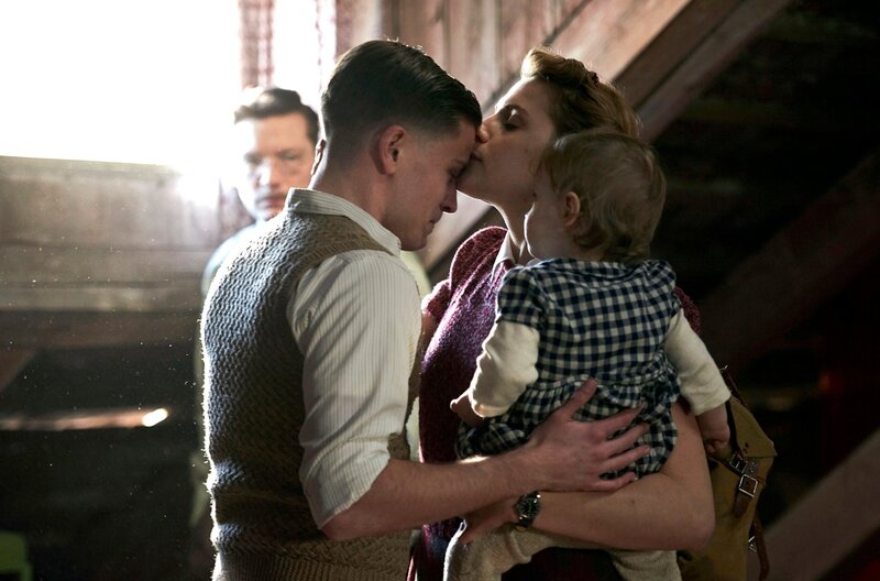 Anni (Mala Emde, r.) hat ihre Tochter aus dem Versteck geholt, ihr Mann Artur (Artjom Gilz, l.) ist überglücklich, Karin nach so langer Zeit in seine Arme schließen zu können. im HG Martin Gruber (Jacob Matschenz). – Bild: ARD/​Julie Vrabelova