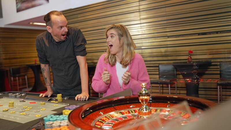 Deswegen treffen Katjana und er sich in einem Kasino. Dort sprechen sie über Risiko und Geuters Kritikpunkte. Katjana hofft auf ihr Glück. Jürgen Geuter sagt, er habe zu viele Mathevorlesungen besucht, um an Glücksspiel zu glauben. – Bild: Jonny Mueller-Goldenstedt /​ ZDF