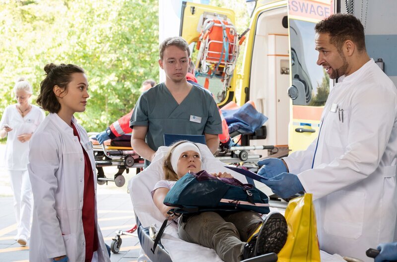 Nach einem Wanderunfall kommt Nadine Bütow (Tina Schorcht, M. mit Komparse) mit einem offenen Bruch ins Klinikum. Moreau (Mike Adler, r.) und Rebecca (Milena Straube, l.) übernehmen die Patientin. – Bild: ARD/​Jens Ulrich Koch