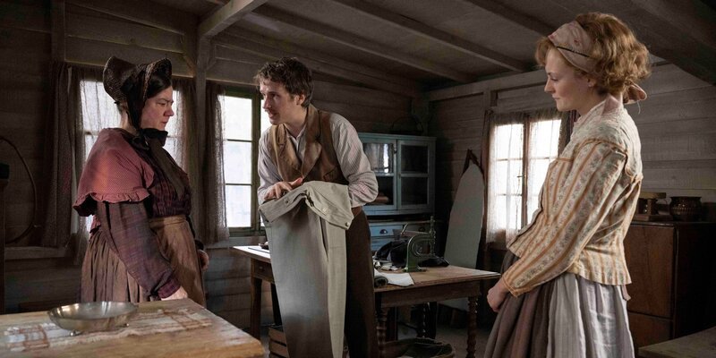 Jacob (Anton von Lucke, Mitte) und Annie (Lea van Acken, re.) versuchen, die selbstgeschneiderten Hosen unter die Mrs. Johnson (Bärbel Schwarz) zu verkaufen und damit an die Tagelöhner zu bringen. – Bild: Martin Rattini