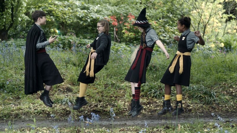 Olli, der richtig Oliver heißt (Milo Panni, links), spielt den drei Freundinnen Maude, Mildred und Edith (Megan Hughes, Bella Ramsey und Tamara Smart) ein Lied von Esper Vespertilios Platte vor. Er würde so gerne auch singen lernen, doch das ist an Schulen für Zauberer verboten. – Bild: BBC/​ZDF Enterprises/​James Stack