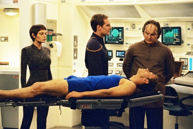 Die Enterprise-Crew, vor allem T’Pol (Jolene Blalock, l.), Captain Archer (Scott Bakula, M.) und Dr. Phlox (John Billingsley, r.) sorgen sich um Tucker (Connor Trinneer, liegend), der nach einem Einsatz auf einem Alien-Raumschiff seltsame Krankheitssymptome zeigt … – Bild: CBS Studios Inc.; Paramount Pictures; SYFY