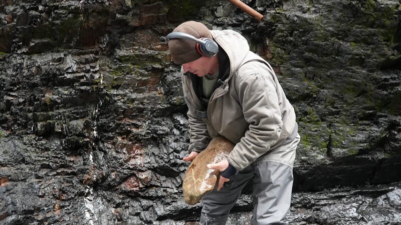 Dustin Hurt moving a large rock in the raging white water. – Bild: Warner Bros. Discovery, Inc. or its subsidiaries and affiliates