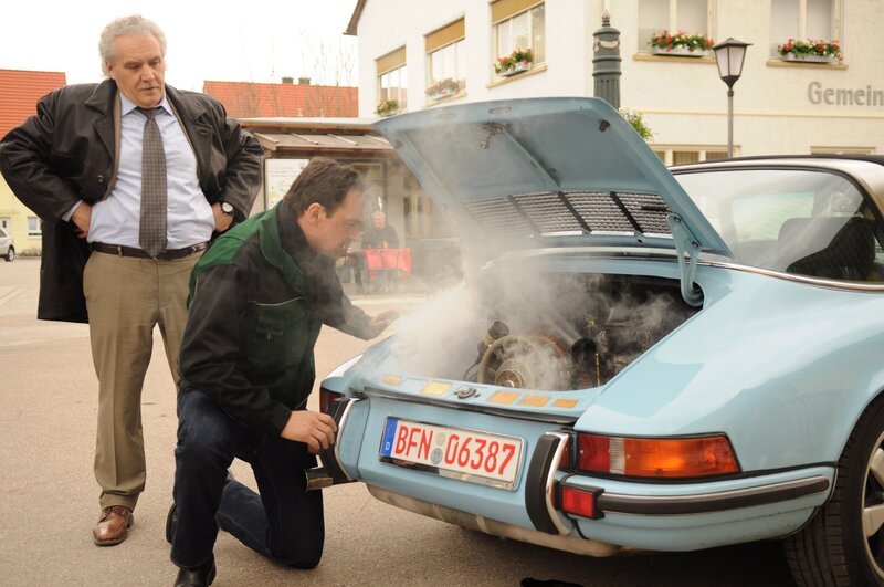 Mike versucht den Fehler beim Auto so schnell wie möglich zu beheben. Von links: Kunde Herr Frei (Bartholomäus Sailer) und Mike Preissinger (Harry Blank). – Bild: BR/​Jo Bischoff