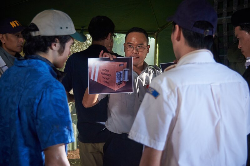 HAMILTON, ONTARIO – Ein indonesischer Ermittler (gespielt von Jon De Leon) übergibt dem Suchtrupp Bilder der Flugschreiber von Garuda Flug 152. (Bildnachweis: Cineflix/​Steven Lungley) – Bild: The National Geographic Channel