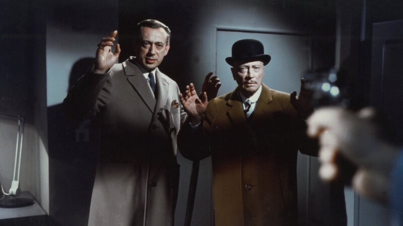 Inmitten der drängenden Ermittlungen zu einer Serie grausamer Mordfälle sehen sich Inspektor Perkins (Horst Tappert, l.) und Sir Arthur (Hubert von Meyerinck, r.) von Scotland Yard plötzlich einer gefährlichen Situation gegenüber, als sie von jemandem mit einer Waffe bedroht und gezwungen werden, ihre nächsten Schritte mit äußerster Vorsicht zu planen. – Bild: ZDF und Constantin Film