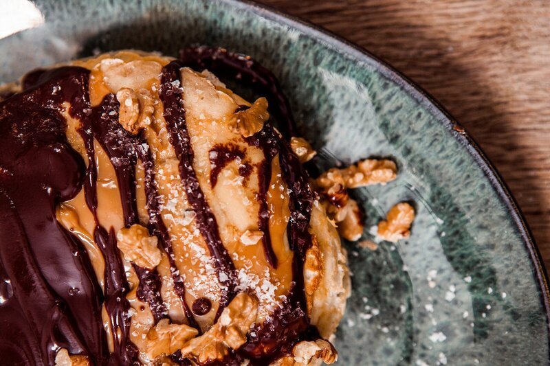 Vögala sind das „Wohlfühlessen“ von Andrea Drey aus dem Raum Günzburg. Die kleinen Nester aus Schnittlauch-Pfannkuchen mit einer Füllung aus Brät sind ein altes schwäbisches Rezept, das schon ihre Oma gern zubereitet hat. Vroni Lutz inspirieren die Vögala zu einem Auflauf aus gefüllten Basilikum-Pfannkuchen mit einer Ricotta-Spinat-Mischung, gebacken in Tomaten-Sauce. Dann wird es richtig süß: Als Dessert kredenzt Vroni eine Art Torte aus Bananen-Pfannkuchen, mit Milchkaramell, Schokosoße, Vanilleeis und Walnuss-Topping (im Bild). – Bild: BR/​Sebastian Fery