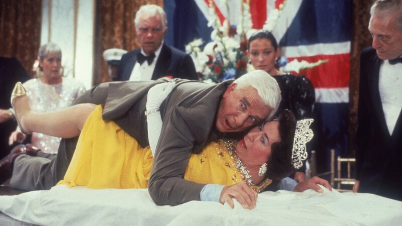 Der ungeschickte Lt. Frank Drebin (Leslie Nielsen, oben) versucht ein Attentat auf die britische Königin Elizabeth II. (Jeannette Charles, unten) zu vereiteln. – Bild: ZDF und Elliott Marks Der ungeschickte Lt. Frank Drebin (Leslie Nielsen, oben) versucht ein Attentat auf die britische Königin Elizabeth II. (Jeannette Charles, unten) zu vereiteln. – Bild: ZDF und Elliott Marks