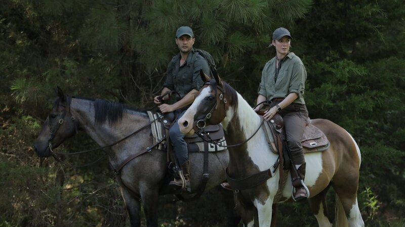 Phil T. and Heather A. ride horses through the forest. – Bild: Warner Bros. Discovery, Inc. or its subsidiaries and affiliates. All rights reserved.