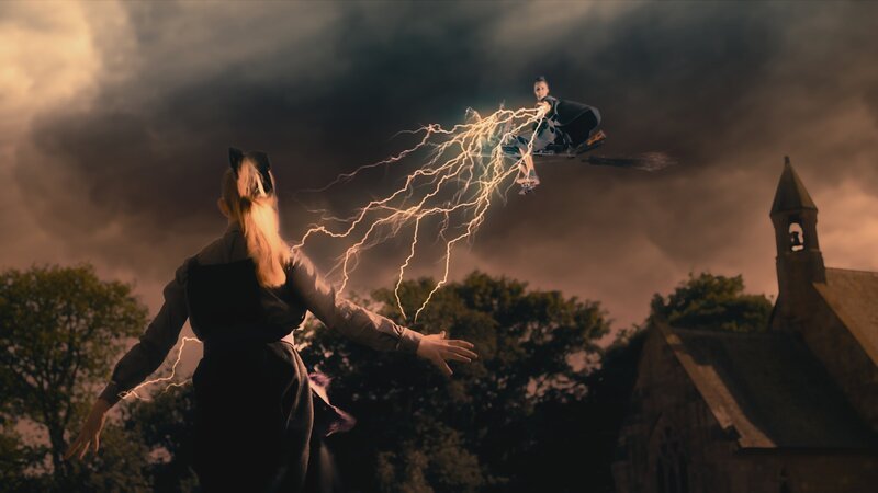 Esther (Jenny Richardson, l.) traut sich gegen die bedrohliche Indigo (Kelsey Calladine-Smith, r.) anzutreten, dafür hat sie sich mit einem Schutzzauber gegen die Blitze abgeschirmt. – Bild: ZDF/​CBBC/​ZDF Enterprises