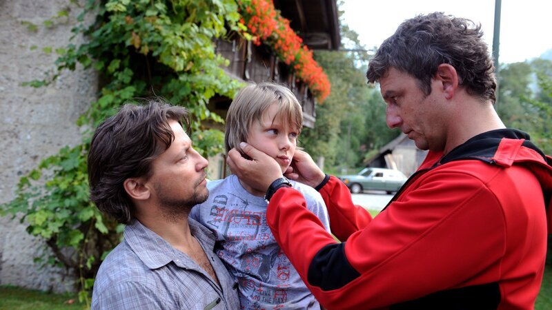 Der kleine Philipp (Vincent Mauz, M.) wirkt gesundheitlich angeschlagen. Doch während Stefans (Patrick Bach, l.) Frau Melanie nach einem Blitzschlag im Krankenhaus um ihr Leben kämpft, wird dies zur Nebensache – auch für Bergdoktor Martin Gruber (Hans Sigl, r.). – Bild: ZDF und Thomas R. Schumann