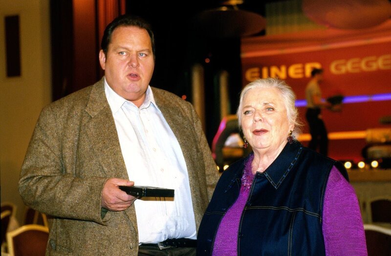 Die TV-Quiz-Show „Einer gegen alle“ wird diesmal in der Tölzer Stadthalle aufgezeichnet. Resi (Ruth Drexel, r.) hofft, dass der bekannte Showmaster Claus Claasen bei ihr wohnen wird, doch Benno (Ottfried Fischer, l.) vermutet richtig, dass Claasen im besten Hotel von Tölz absteigt. Am nächsten Morgen wird in Claasens Hotelzimmer eine Leiche gefunden, und sofort verbreitet sich die Nachricht, der Showstar sei ermordet worden. – Bild: SAT.1 /​ Magdalena Mate