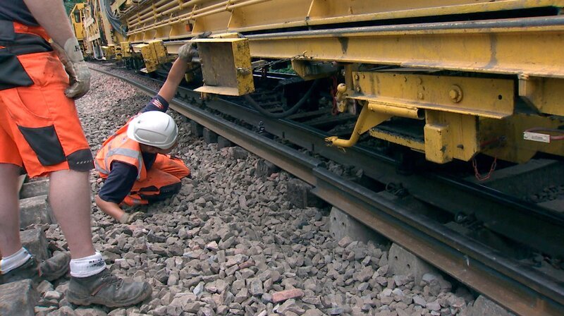 Arbeiter kontrollieren die Genauigkeit des Gleisumbauzuges – Bild: SWR