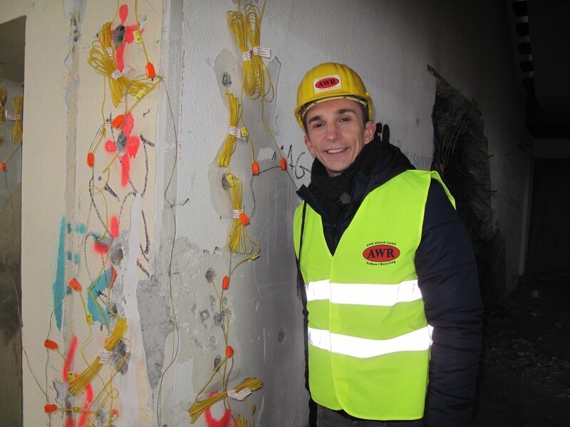 pur+-Moderator Eric Mayer vor einer mit Sprengsätzen präparierten Wand. – Bild: ZDF/​Carina Schulz