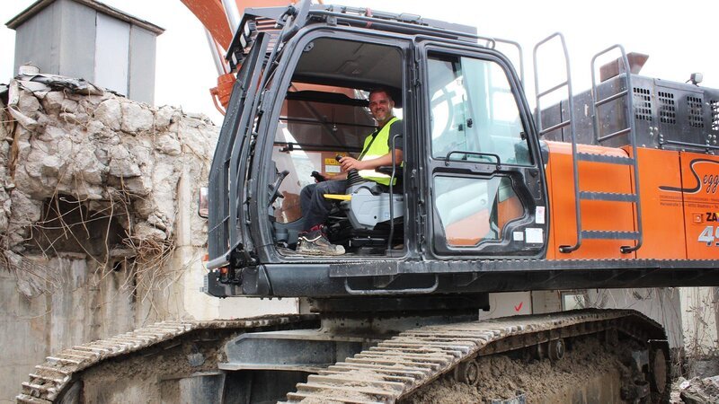 Arbeiter in einem Bagger während des Abrisses. – Bild: Warner Bros. Discovery