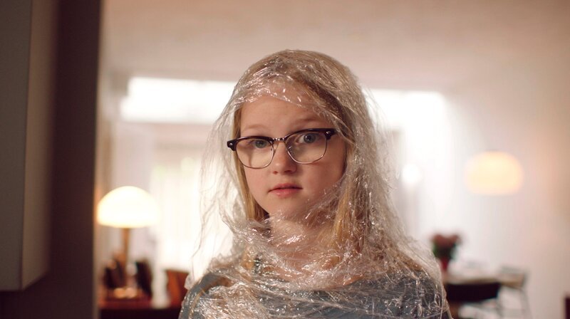 Im selbstgemachten Schutzanzug sieht Floor (Bobbie Mulder), dass Margreet viele Geschenke bekommt, weil sie krank ist. – Bild: NDR/​NL Film