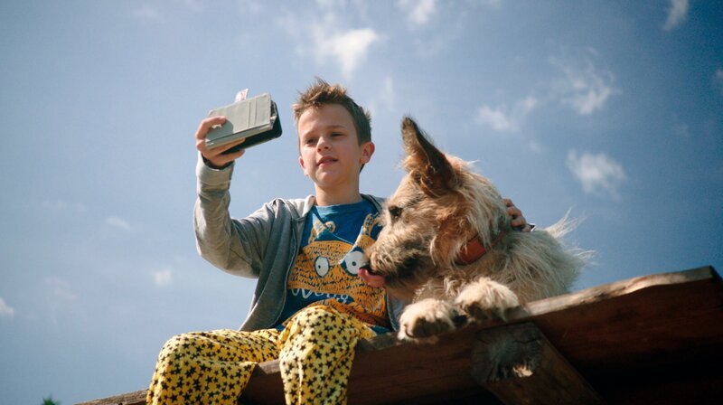Flori (Leon/​Lino de Greiff) mit seinem Racko. Flori nimmt eine Videobotschaft für Herrn Angerer auf. – Bild: BR/​Filmbüro Münchner Freiheit GmbH