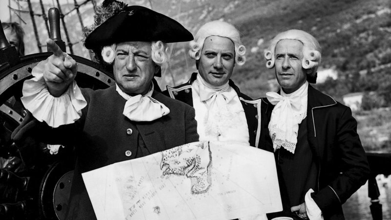 Die Hispaniola ist vor der Schatzinsel angelangt. Kapitän Smollet (Jacques Monod, l.) erläutert Trelawney (Jacques Dacquemine, m.) und Dr. Levesey (Georges Riquier, r.) anhand der alten Karte des Seeräubers Flint die Einfahrt in die Ankerbucht. – Bild: 3sat