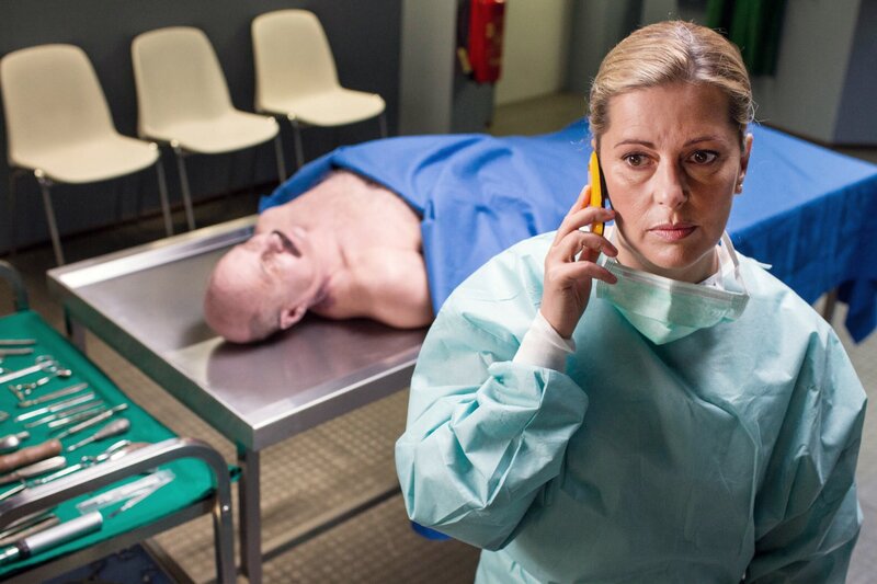 Dr. Anja Licht (Karin Thaler) hat bei der Obduktion des toten Polizisten (Komparse) eine seltsame Entdeckung gemacht und teilt diese Hubert und Staller per Telefon mit. – Bild: ARD/​ARD/​TMG/​Chris Hirschhäuser