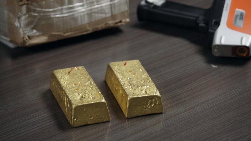 Goldbarren werden auf einen Inspektionstisch gelegt, während HSI-Agenten in der Nähe eine Nachbesprechung über einen untersuchten illegalen Goldabbau in Miami durchführen. – Bild: NGC NETWORK US, LLC