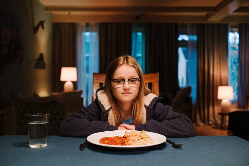 Floor (Bobbie Mulder) sitzt am Tisch während Kees über ihr Abendessen vloggt. – Bild: KiKA