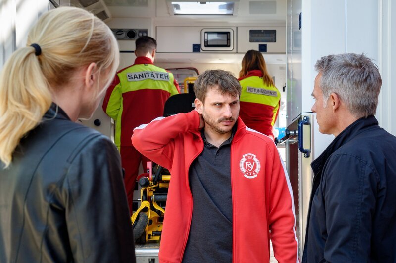 Ina Zimmermann (Melanie Marschke, l.) und Jan Maybach (Marco Girnth, r.) sprechen mit Rico Schäfer (Felix Bold, M.), der gerade notärztlich untersucht wurde. – Bild: ZDF und Uwe Frauendorf