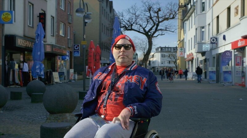 Niko Brenner, alias Dr. Knarf, fährt in seinem Rollstuhl durch Köln-Porz. – Bild: WDR/David Klammer Niko Brenner, alias Dr. Knarf, fährt in seinem Rollstuhl durch Köln-Porz. – Bild: WDR/David Klammer