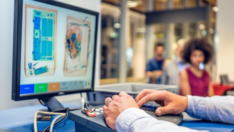 In foreground is computer monitor with luggage image, incidental people in background. – Bild: Model and Property Released (MR&PR)