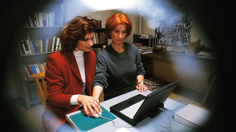 Jeanette beobachtet durch den Türspion, wie Evelyn (Franziska Matthus, li.) Regine (Ana Fonell) eine Computereinführung gibt und sieht auch, wo Regine ihr Manuskript versteckt hat. – Bild: RTL