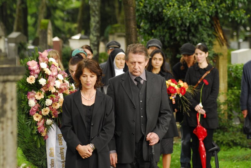 Das Ehepaar Eva und Max Täschner ist zur Beerdigung ihres ehemaligen Au-Pair-Mädchens gekommen. Die stark verweste Leiche der jungen Frau hatte man Tag zuvor in der Nähe eines Tümpels gefunden. – Bild: BR/​Manfred Lämmerer