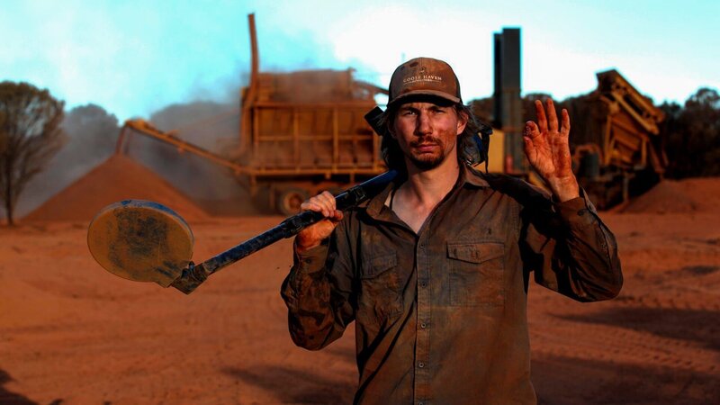 Parker Schnabel holding a piece of gold, covered in red dust. Similar shot as above but wider – Bild: Discovery Communications, LLC