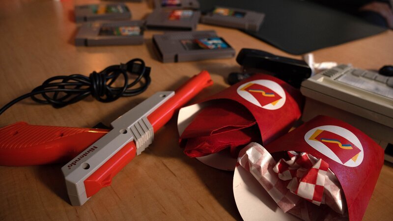 Retro-Videospiele, eine Plastikpistole und Essensverpackungen liegen auf einem Tisch. – Bild: The HISTORY Channel