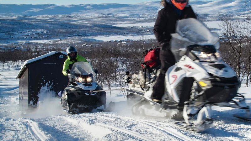 Zwei Schneemobile rasen durch die verschneene Wildnis und transportieren Ausrüstung sowie eine kleine Hütte über weiße Spuren. – Bild: Waidwerk