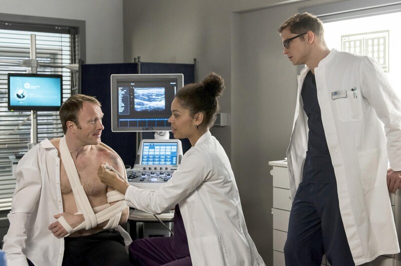 Nach dem Einrenken untersuchen die Ärzte Bernd Müllers Schulter per Ultraschall – und machen eine unschöne Entdeckung. V.l.n.r. Bernd Müller (Merten Schroedter), Vivienne Kling (Jane Chirwa), Elias Bähr (Stefan Ruppe). – Bild: Jens-Ulrich Koch