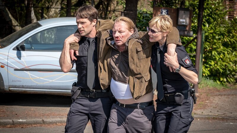 Mattes (Matthias Schloo, l.) und Melanie (Sanna Englund, r.) bringen Heinrich Frank (Ben Becker, M.) zum Rettungswagen. Er muss dringend medizinisch versorgt werden. – Bild: ZDF